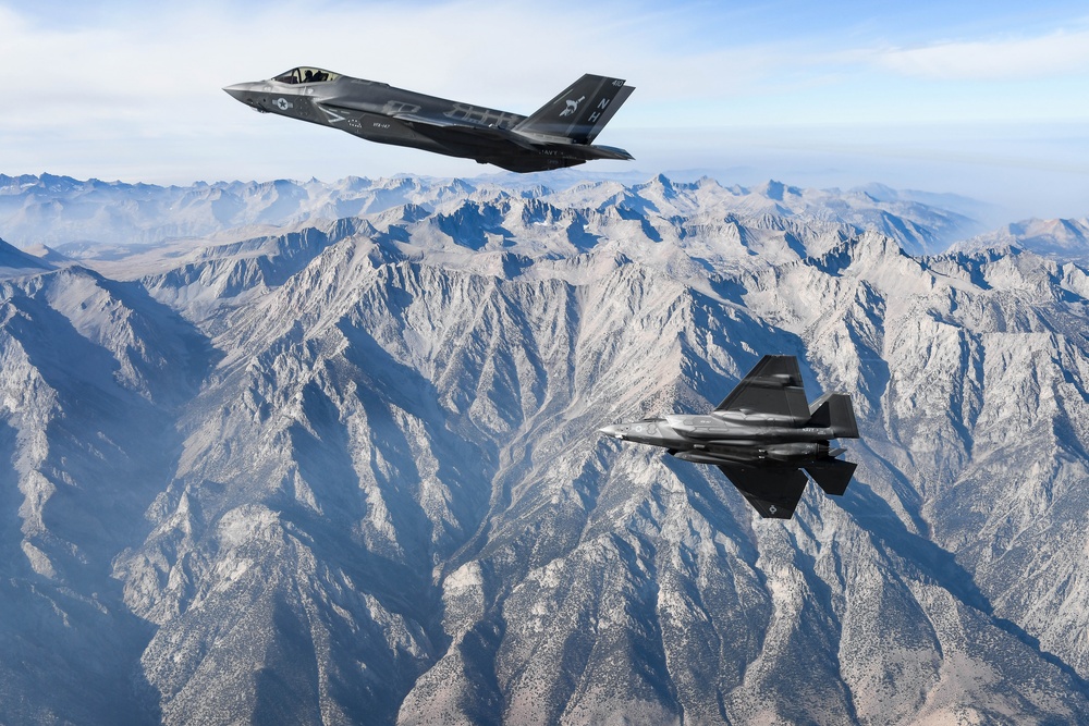 Two military jets in flight over mountains