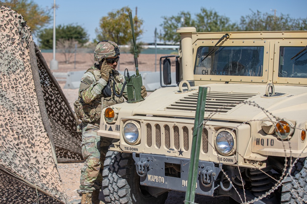 Soldier speaking on a handset radio beside a tactical vehicle